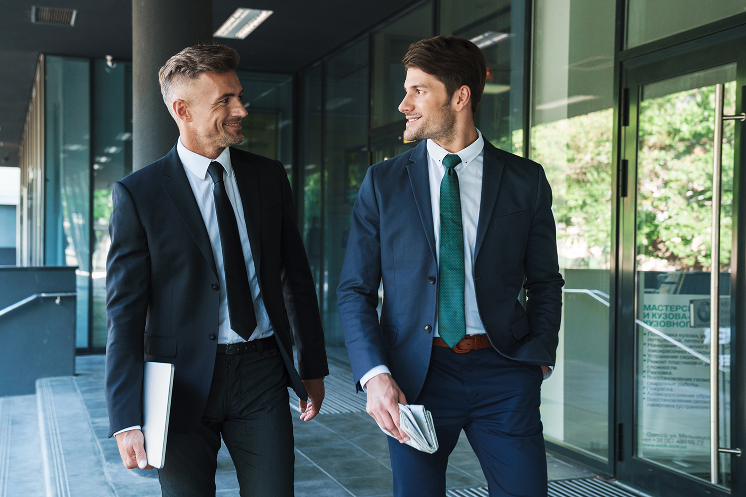 Two businessmen make plans outside of a corporate office building.